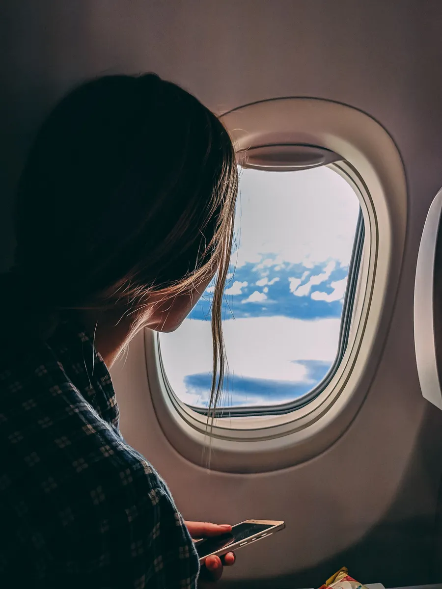 Viajero revisando su teléfono junto a la ventanilla de un avión